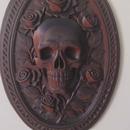 Decorative wall plaque with a skull and floral design on a white background