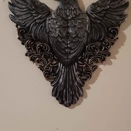 Decorative wall piece with winged black bird design on a beige background